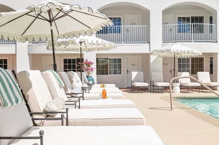 Elegant poolside lounge with white umbrellas, cushioned chairs, and whitewashed coastal buildings