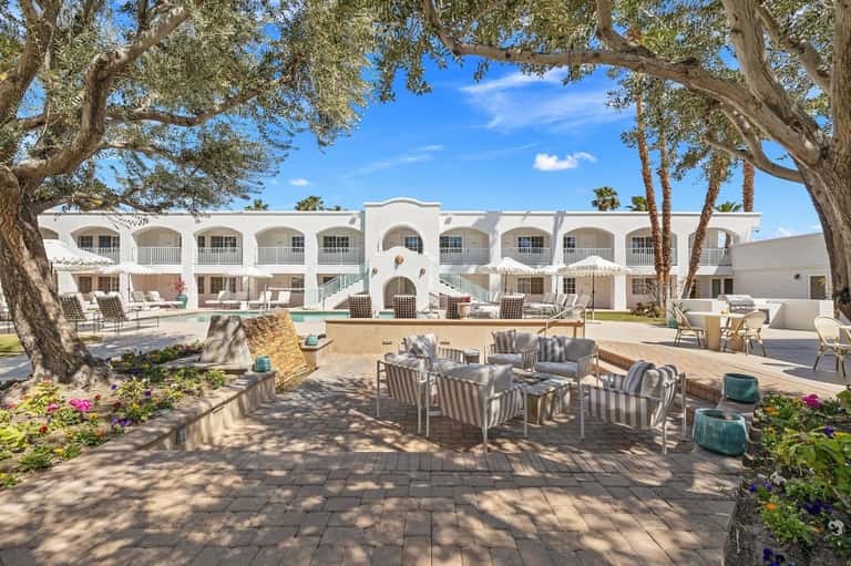 Resort courtyard with white building, swimming pool, lounge chairs, and mature trees