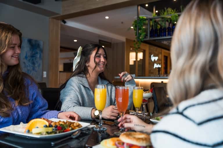 Three women enjoying brunch with mimosas and fresh fruit at an indoor hotel restaurant