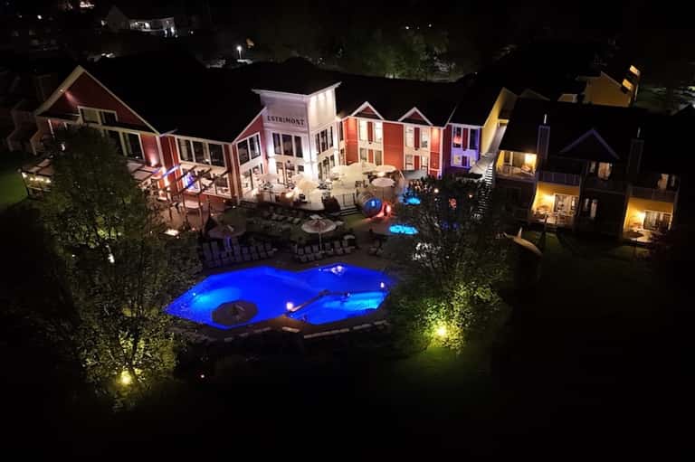 Nighttime aerial view of colorful resort buildings with illuminated pool and outdoor seating areas