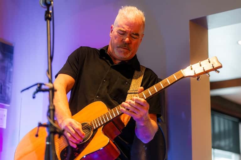 Musician performing with acoustic guitar on stage with purple lighting