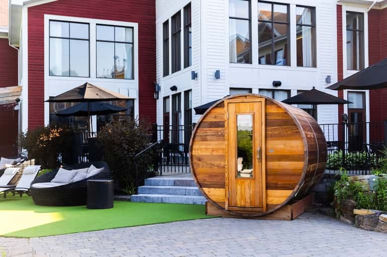 Modern residential backyard with wooden barrel sauna, black umbrellas, lounge chairs, and contemporary architecture