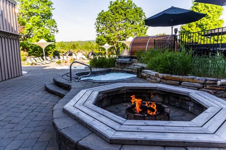 Resort fire pit on patio with hot tub, lounge chairs, umbrella, and hillside landscape views