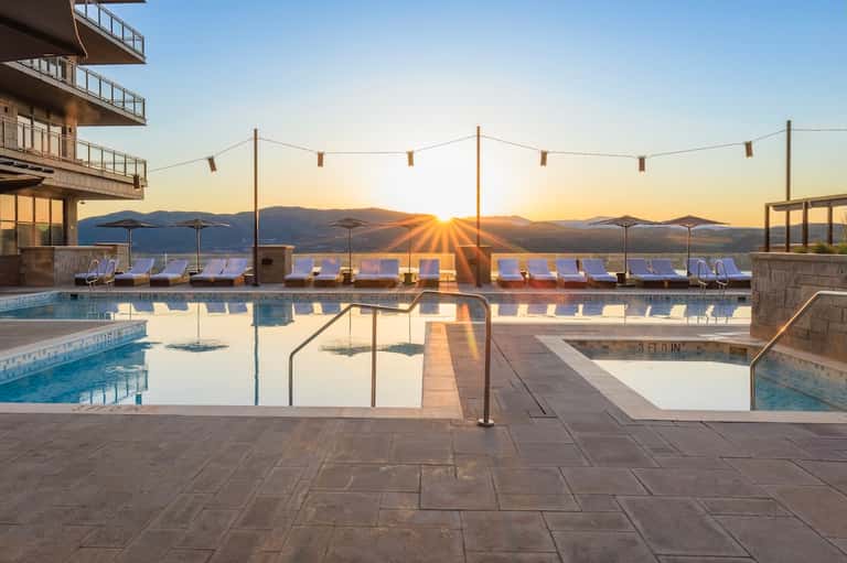 Resort infinity pool at sunset with mountain views, lounge chairs, umbrellas, and modern architecture silhouetted