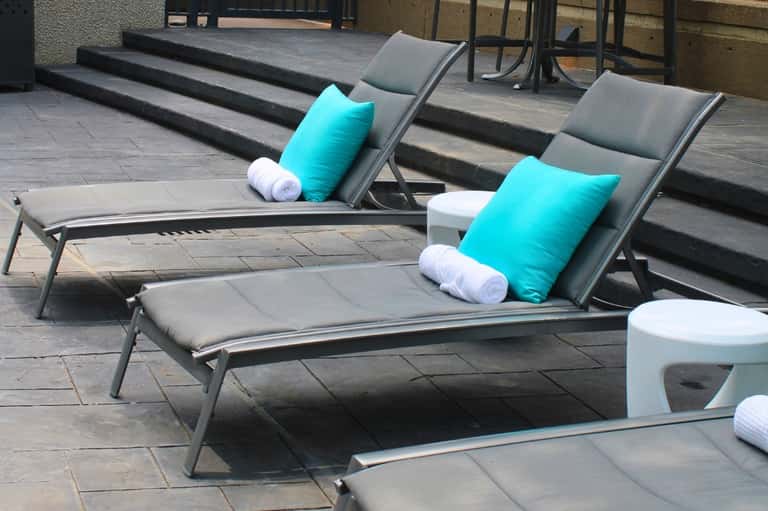 Outdoor lounge chairs with turquoise pillows and white towels on tiled terrace overlooking steps