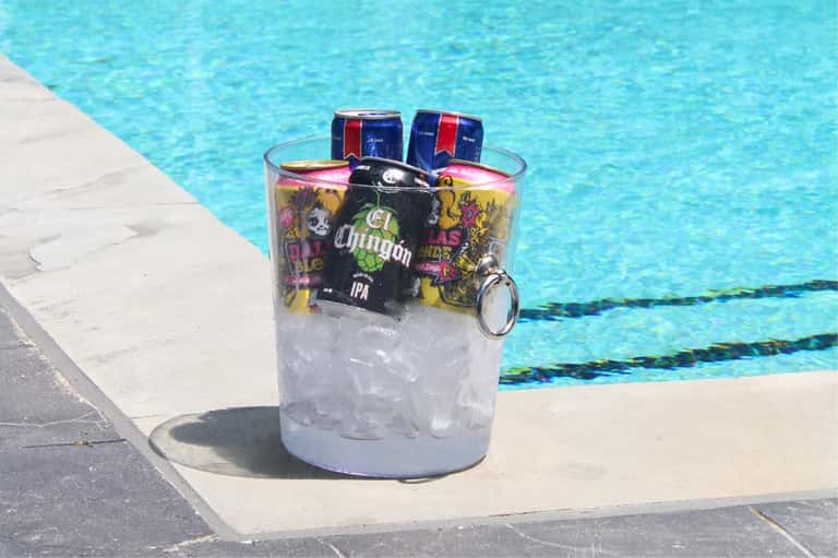 Poolside beverage holder with ice and beers on a white deck beside bright turquoise water