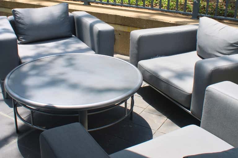 Outdoor terrace seating area with gray upholstered chairs and round metal table on sunny patio