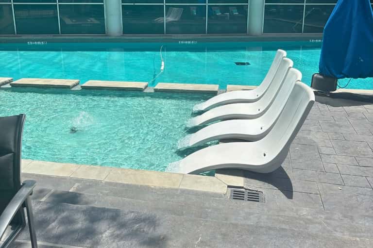 Indoor swimming pool with turquoise water and white curved lounge chairs along the edge