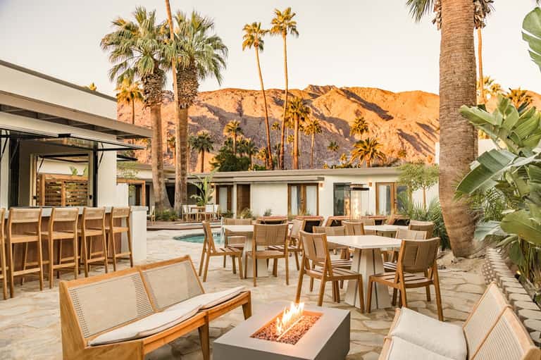 Desert resort patio with palm trees, fireplace, dining area, and mountain views