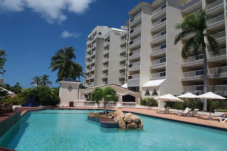 Resort pool with turquoise water, palm trees, white umbrellas, and multi-story hotel building backdrop