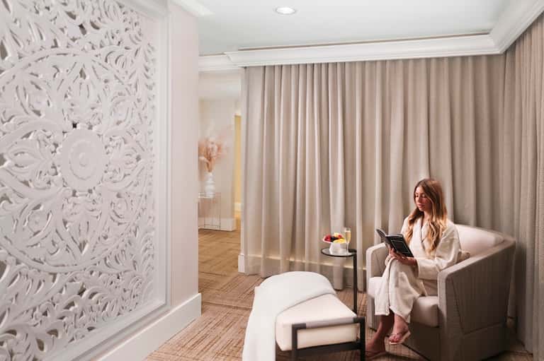 Luxurious spa relaxation room with ornate white wall panel and woman reading in chair