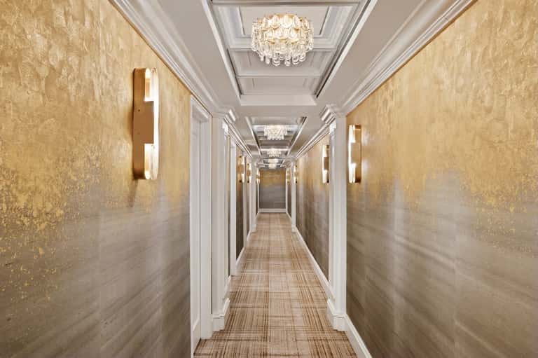 Elegant hallway with gold textured walls, white trim, and crystal chandeliers