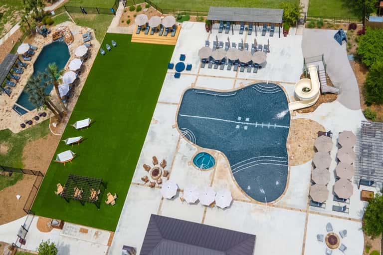 Aerial view of resort complex with multiple pools, loungers, and manicured green lawn