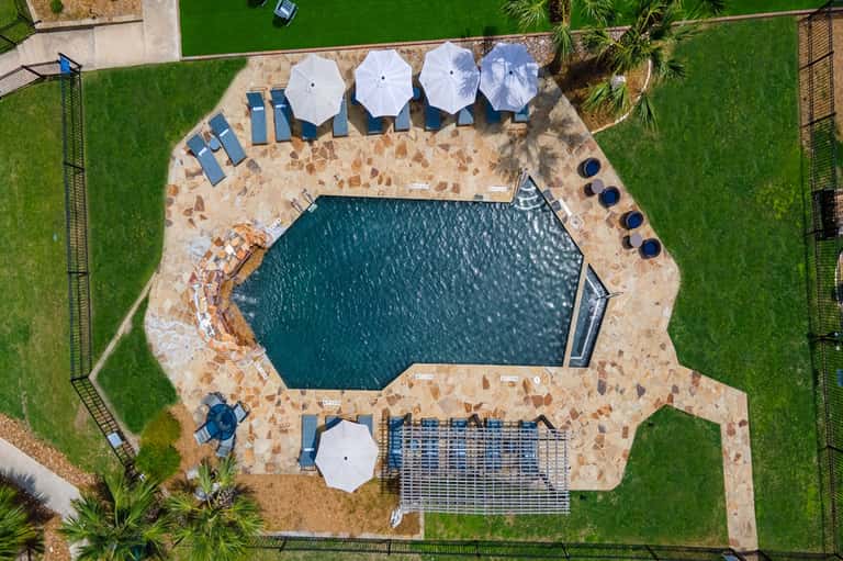 Aerial view of freeform pool with white umbrellas, lounge chairs, and manicured lawn surroundings