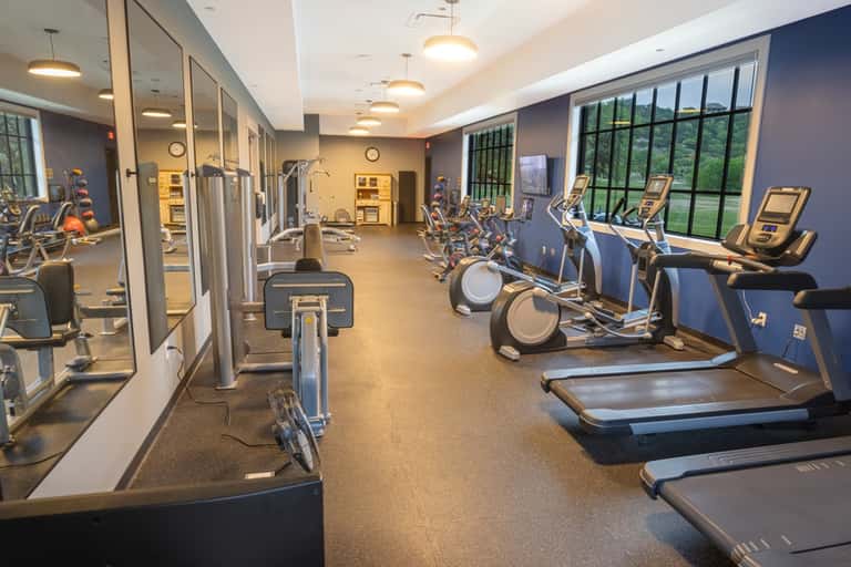 Modern fitness facility with stationary bikes, treadmills, mirrors, and large windows overlooking grounds