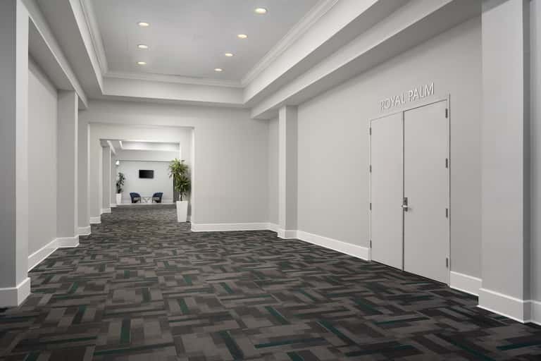 Modern hotel hallway with geometric floor pattern, white walls, recessed lighting, and Royal Palm signage