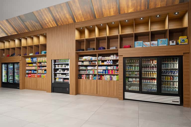 Modern retail shop interior with wooden shelving, refrigerated beverage displays, snack products, and organized merchandise