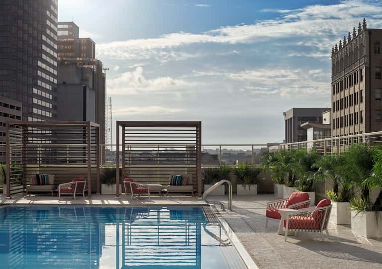 Urban rooftop pool with lounge chairs, pergolas, and city skyline views at daytime