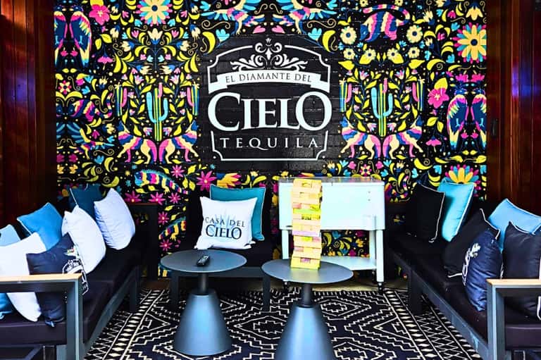 Vibrant lounge space with colorful floral wallpaper, El Diamante del Cielo Tequila branding, blue seating, and decorative pillows