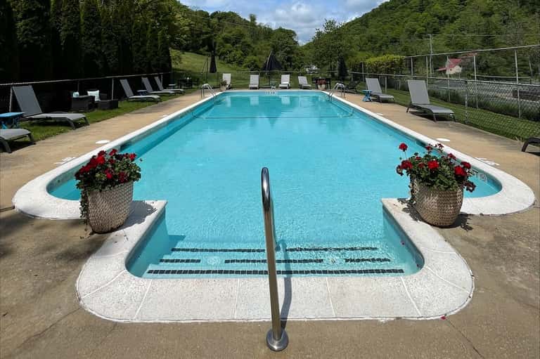 Resort lap pool with red flower planters, lounge chairs, umbrellas, and green hillside backdrop