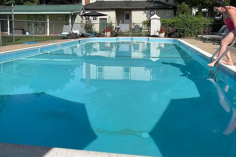Residential community pool with crystal blue water, white diving board, cottages, and green lawn areas