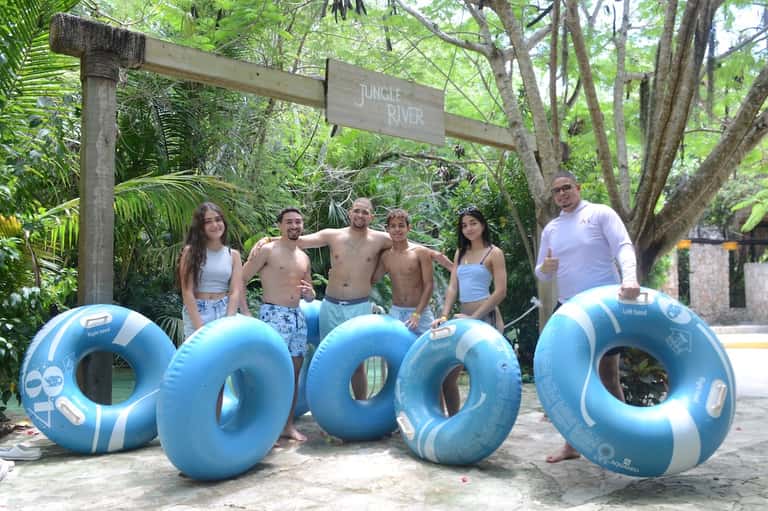 Group of six people with floats at jungle river attraction entrance surrounded by lush tropical trees