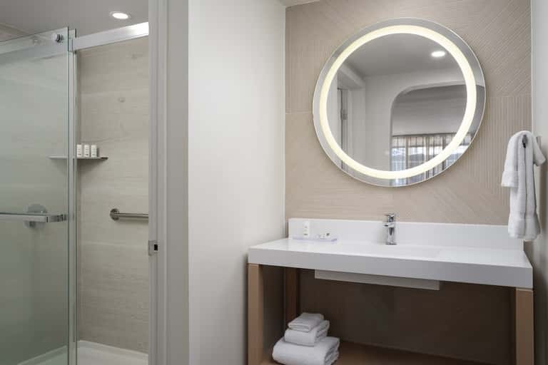 Modern bathroom with illuminated circular mirror, walk-in shower, and neutral tones