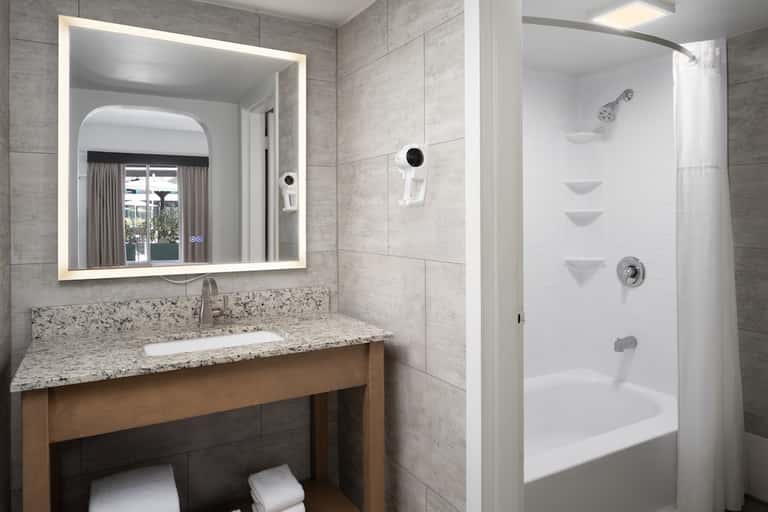 Modern hotel bathroom with granite countertop, lit mirror, and walk-in shower
