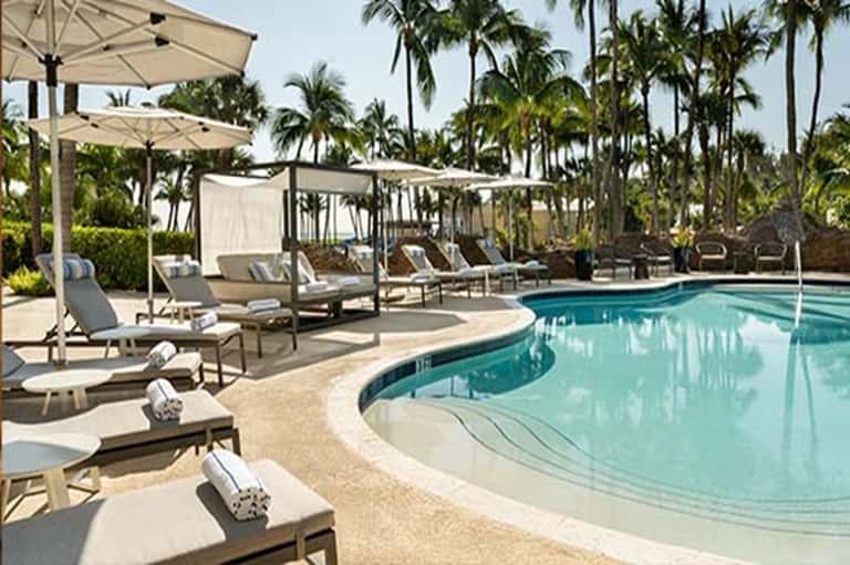 Resort swimming pool surrounded by lounge chairs, umbrellas, and tropical palm trees