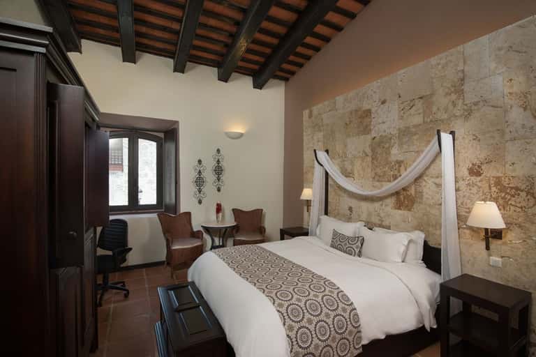 Rustic bedroom with stone accent wall, canopy bed, dark wood beams, and traditional decor