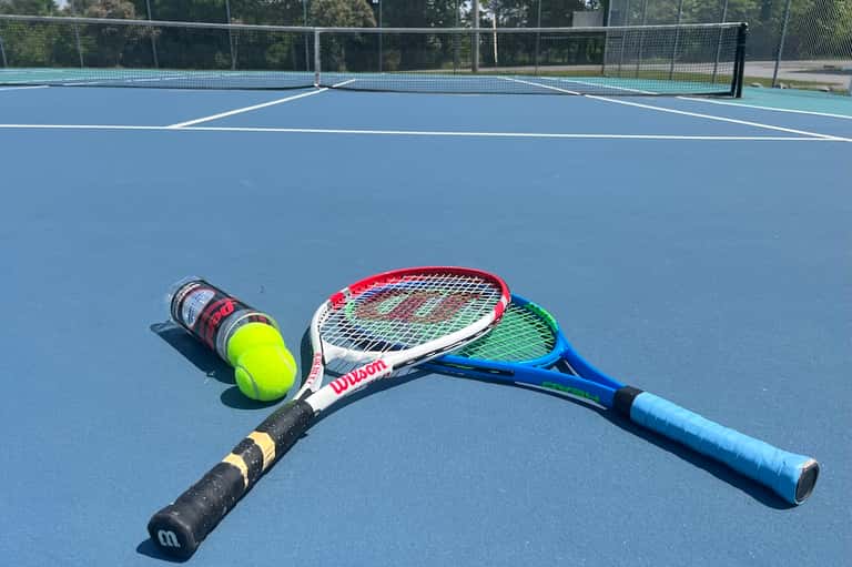 Tennis court with red racket, yellow balls, and net fence under clear sky
