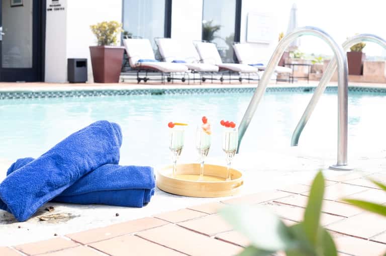 Resort pool with blue towels, champagne glasses, loungers, and palm trees in background