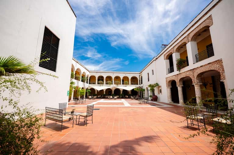 Spanish colonial courtyard with arched walkways, terracotta floor, and planted greenery