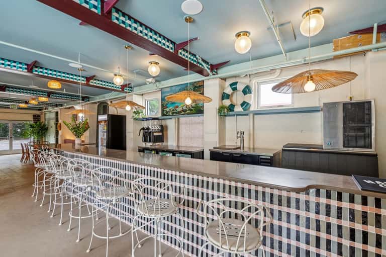 Coastal restaurant with teal ceiling beams, pendant lighting, and breakfast bar seating