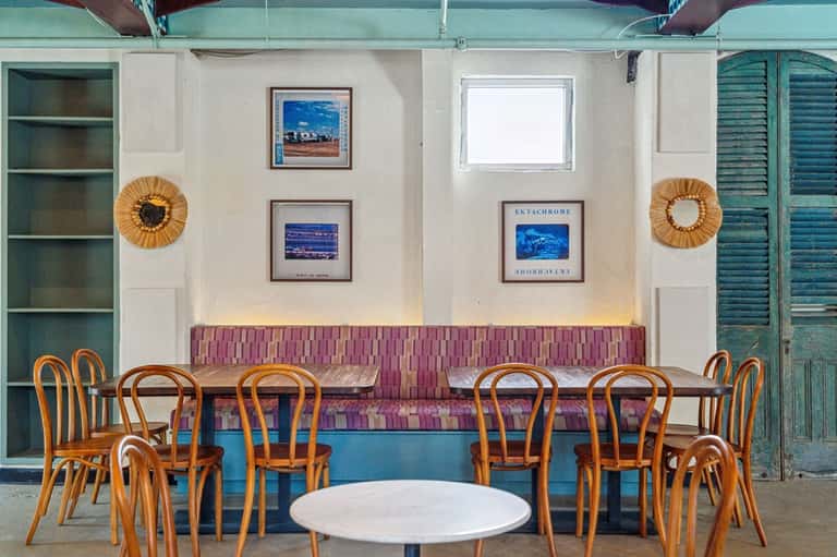 Retro hotel lounge with wooden chairs, purple-pink seating, blue counter, and framed ocean artwork