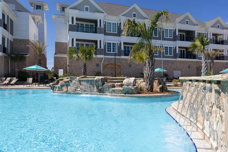 Luxury waterfront resort with white buildings, decorative pool with rock features, and palm trees
