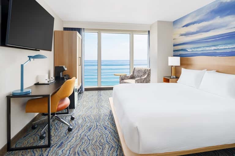 Beachfront hotel room with ocean view balcony, desk workspace, and modern furnishings