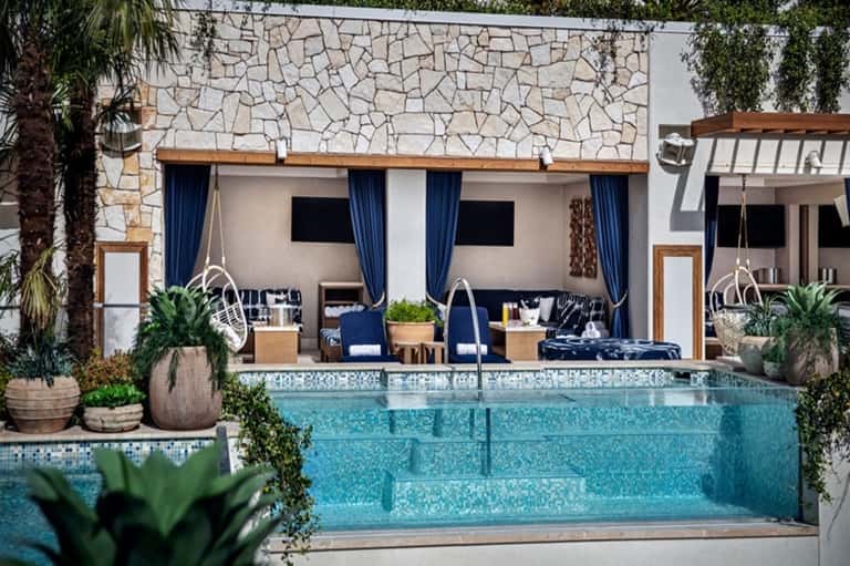 Modern pool cabana with hanging chairs, blue curtains, and stone accent wall