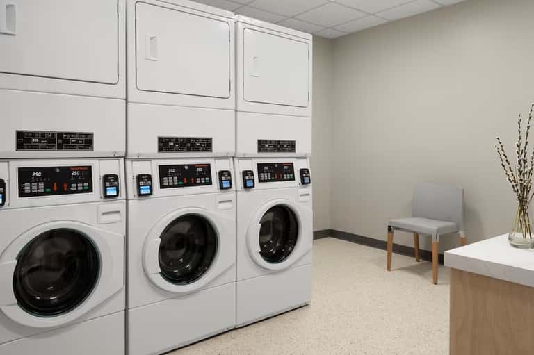 Laundry room with stacked commercial washers, dryers, and waiting seating