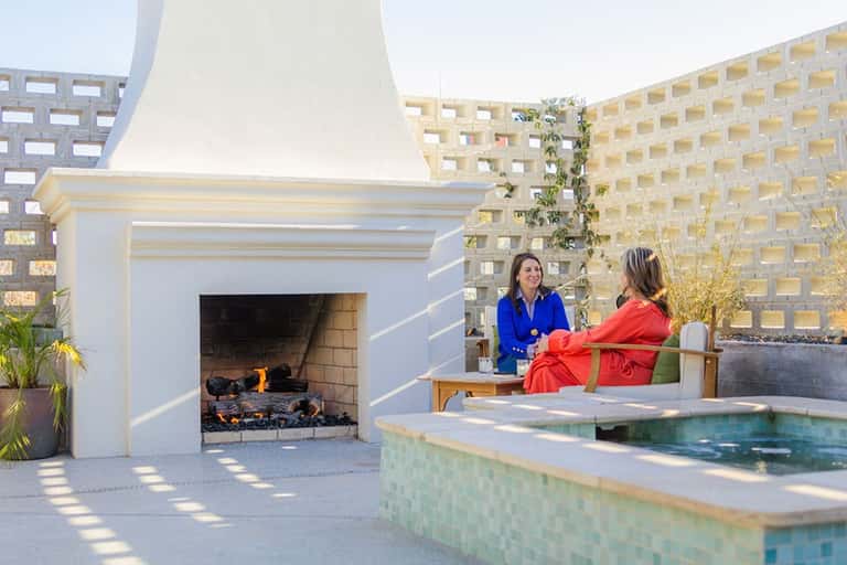 Rooftop fireplace lounge with white architectural features, two women conversing, and water feature