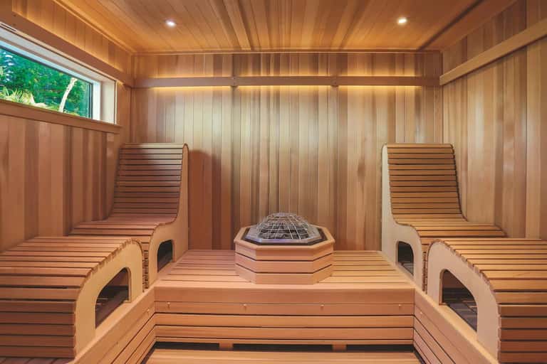 Wooden sauna interior with benches, hexagonal heater, and window overlooking green vegetation