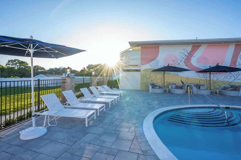 Spa pool area with artistic mural wall, white loungers, umbrellas, and waterfront views at golden hour