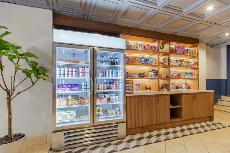 Hotel gift shop with refrigerated cases, illuminated wood shelving displaying merchandise