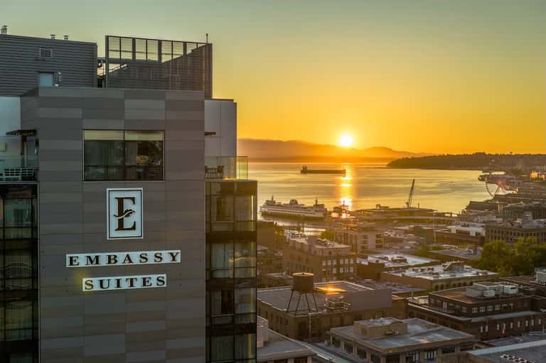 Embassy Suites hotel exterior at sunset overlooking waterfront and city buildings