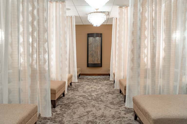 Spa hallway with sheer white curtains, beige seating alcoves, elegant lighting, and artwork