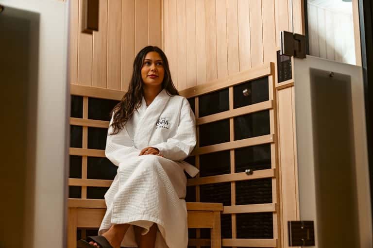 Woman in spa robe standing in modern sauna facility with wooden doors