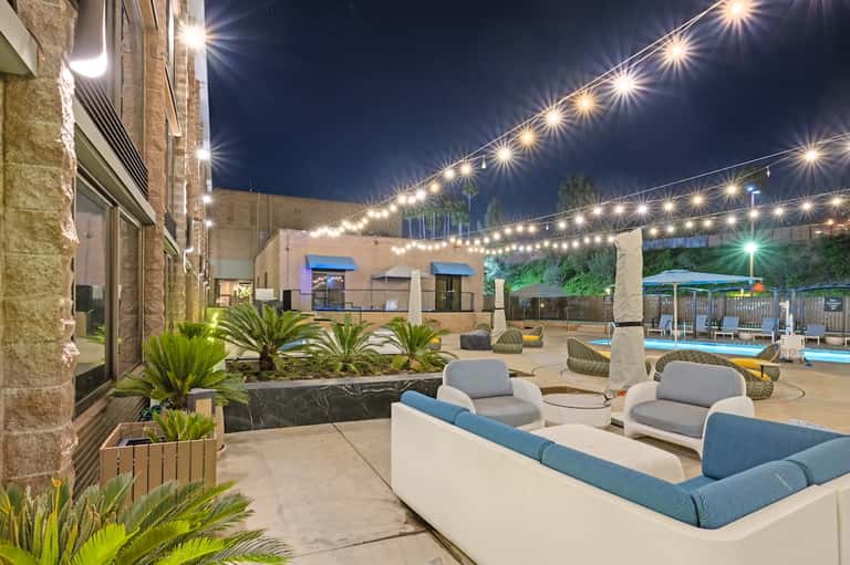 Outdoor courtyard with lounge seating, string lights, and illuminated pool at night
