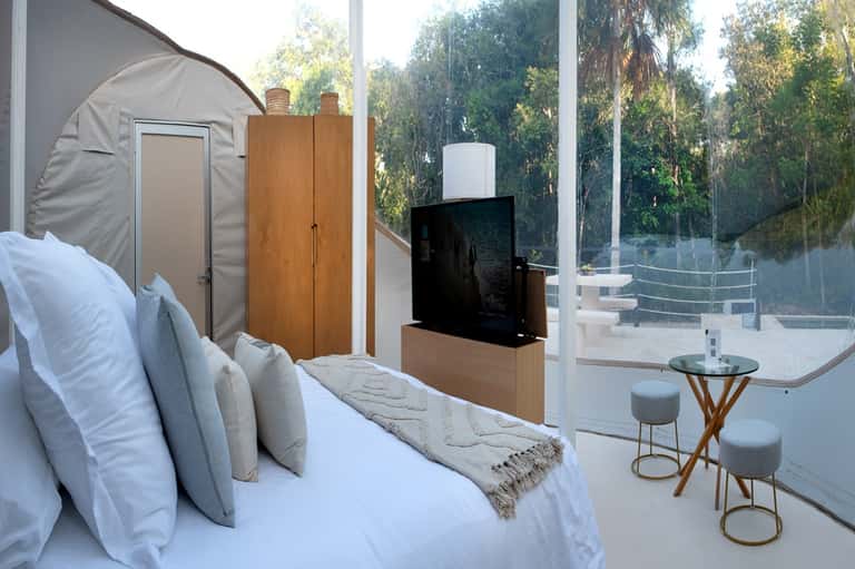 Modern hotel bedroom with platform bed, glass wall access to terrace, TV, and minimalist furnishings