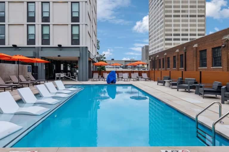 Urban rooftop pool with lounge chairs, orange umbrellas, and surrounding city buildings