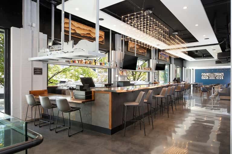 Contemporary hotel restaurant with open kitchen, geometric pendant lights, wood accents, and floor-to-ceiling windows